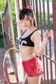 A woman in a black top and red shorts leaning against a fence.