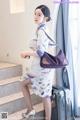 A woman in a cheongsam is standing next to a suitcase.