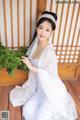 A woman in a white dress sitting on a wooden floor.