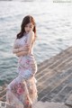 A woman in a floral dress standing by the water.