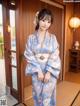 A woman in a blue kimono standing in front of a door.