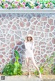 A woman in a white dress and hat posing in front of a wall.