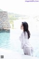 A woman in a white dress sitting by a swimming pool.