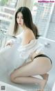 A woman in a white shirt and black panties sitting in a bathtub.