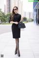 A woman in a black dress is walking down the street.