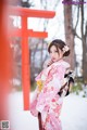 A woman in a pink kimono standing in front of a red torii gate.