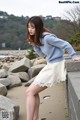 A woman in a blue sweater and a white skirt leaning against a wall.