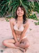 A woman in a white bikini sitting on the sand.