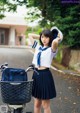 A woman in a school uniform standing next to a bike.